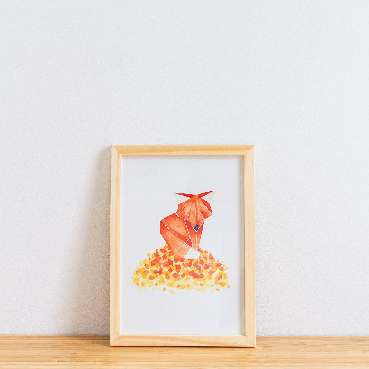 Watercolour painting art print. The watercolour illustration shows an origami autumn fox standing on top of a pile of autumn leaves.