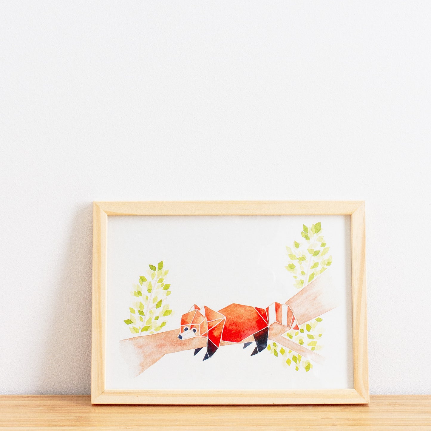 Watercolour painting art print. The watercolour illustration shows an origami red panda lying down on a tree branch with leaves.