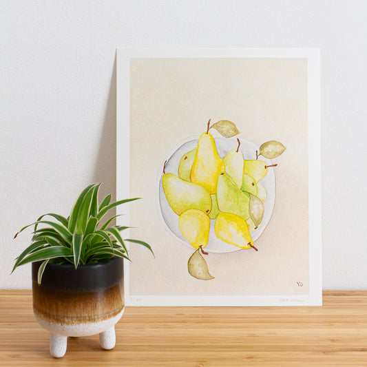 Image is a photo of a Limited edition art print sitting on bamboo wood surface with white background. The print is a reproduction from a handmade watercolour painting representing pears in a grey white bowl from above.