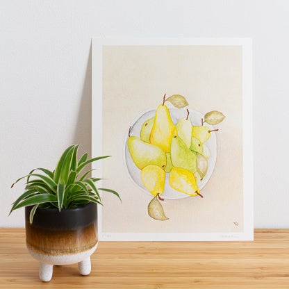 Image is a photo of a Limited edition art print sitting on bamboo wood surface with white background. The print is a reproduction from a handmade watercolour painting representing pears in a grey white bowl from above.