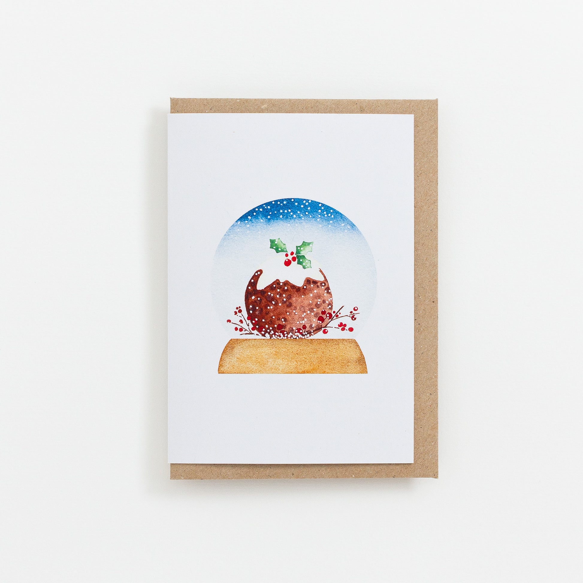 A festive food Snow Globe card designed from handmade watercolour painting. The illustration is a round Christmas pudding topped with icing and holly.