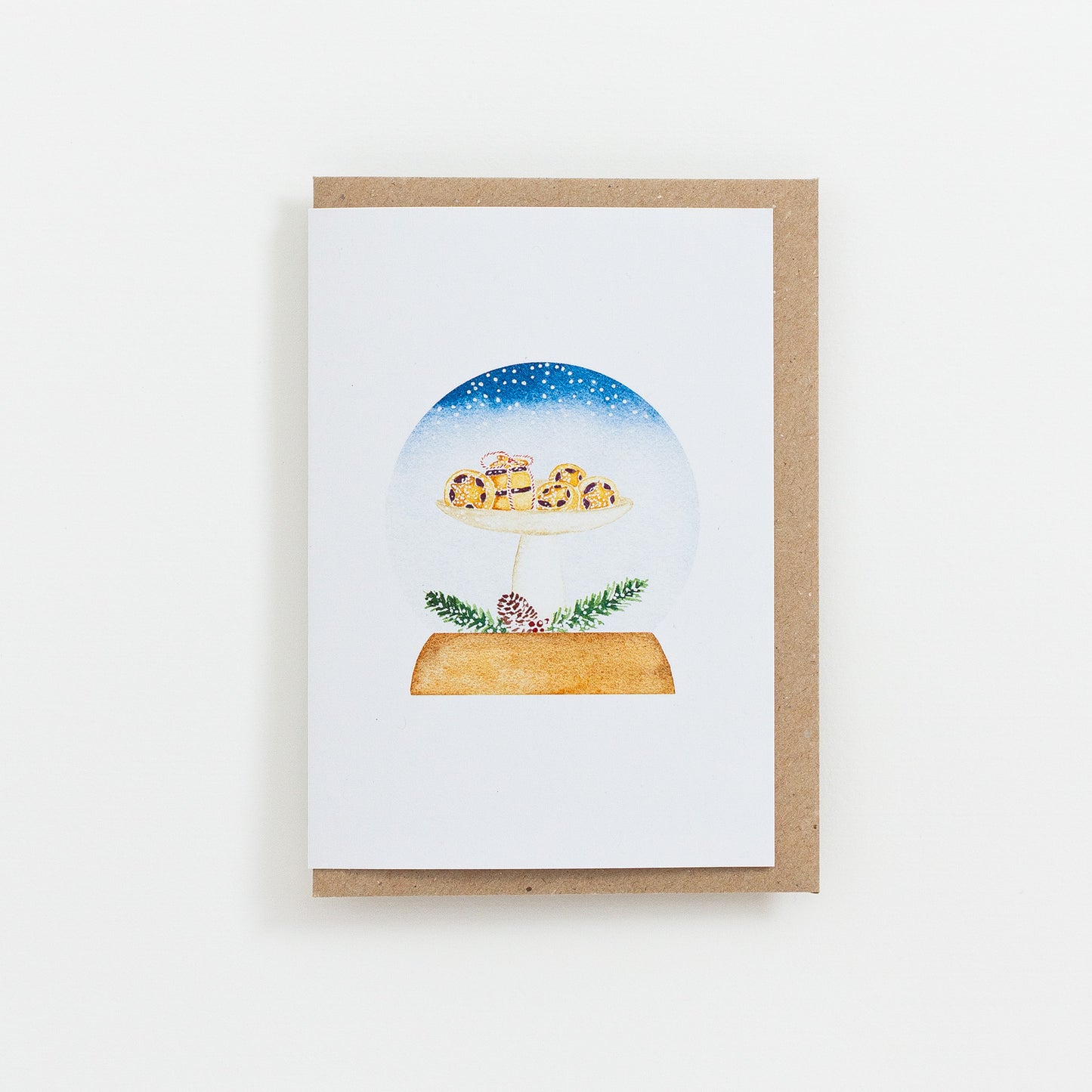A festive food Snow Globe card designed from handmade watercolour painting. The illustration is a tall dish filled with little mince pies dusted with icing sugar.